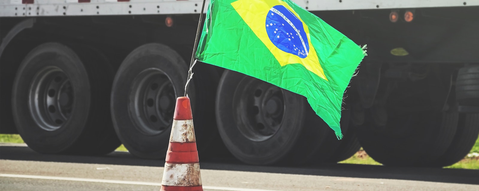 Brazilian flag on a red traffic cone of a highway with a blurred truck on background